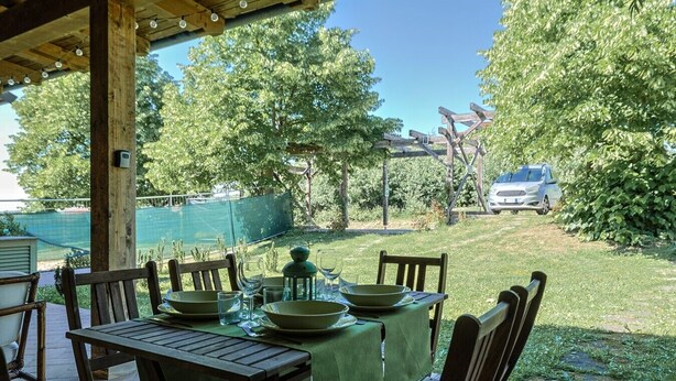 An outdoor patio with a table set for dining, surrounded by chairs, and a covered area with a wooden ceiling.