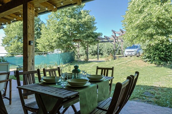 An outdoor patio with a table set for dining, surrounded by chairs, and a covered area with a wooden ceiling.