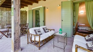 A cozy room with a wooden ceiling, a sofa with animal-themed cushions, a small table with a lantern, and a bed with green curtains. - Lagotto House - Garden and Parking in the Langhe (Novello)