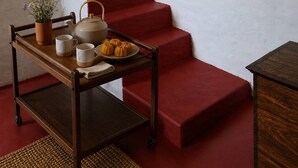 Una escalera con peldaños rojos, una mesa de madera con una bandeja de objetos, y cestas colgantes.