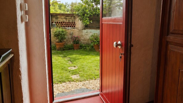 Un pasillo con una puerta roja que da a un jardín.