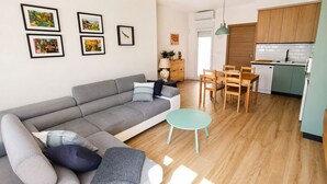 A modern living room with a grey sofa, a round turquoise table, and a dining area with wooden chairs and a kitchen in the background. - Adela House (Maracena)