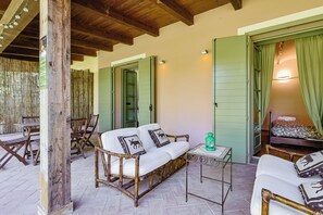 A room with a wooden-framed sofa, a small table, and a bed with green curtains. - Lagotto House - Giardino e Parcheggio nelle Langhe (Piemonte)