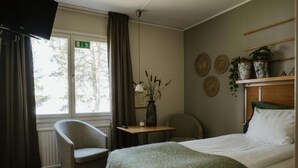 A hotel room with a bed, a chair, a small table with a vase, and a shelf with plants. - Fagerudd (Enköping)