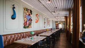 A restaurant with long wooden tables, black chairs, and decorative wall art including peacocks and a flamingo. - Fagerudd (Enköping)