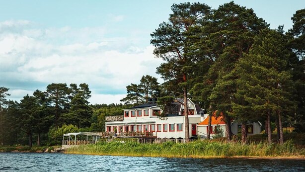 A lakeside house with a large deck, surrounded by trees. - Fagerudd (Enköping)