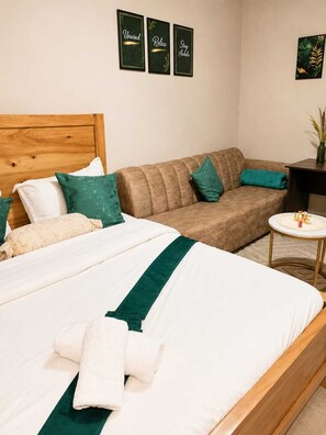 Ein ordentlich eingerichtetes Schlafzimmer mit einem Bett, einer Couch, einem kleinen Tisch und Wandbildern.