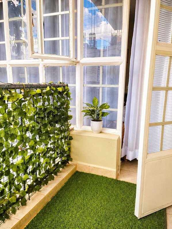 Ein Zimmer mit Fenster, einer Topfpflanze auf einem Sims und einer Fläche mit grünem Kunstrasen.