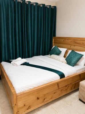 Ein hölzernes Bett mit weißer Bettwäsche, türkisblauen Kissen und einer türkisblauen Decke.