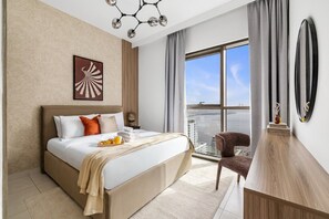A modern hotel room with a large bed, a view of the city, a dining area, and a balcony. - Luxury 3BR with Sea Views & Pool - Creekside (Dubai)