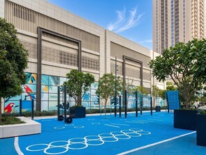 An outdoor fitness area with exercise equipment, trees, and a building with a patterned facade. - Luxury 3BR with Sea Views & Pool - Creekside (Dubai)