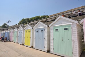 Eine Reihe bunter Strandhäuser mit weißen Fassaden und pastellfarbenen Türen, die entlang einer Strandpromenade aufgereiht sind.