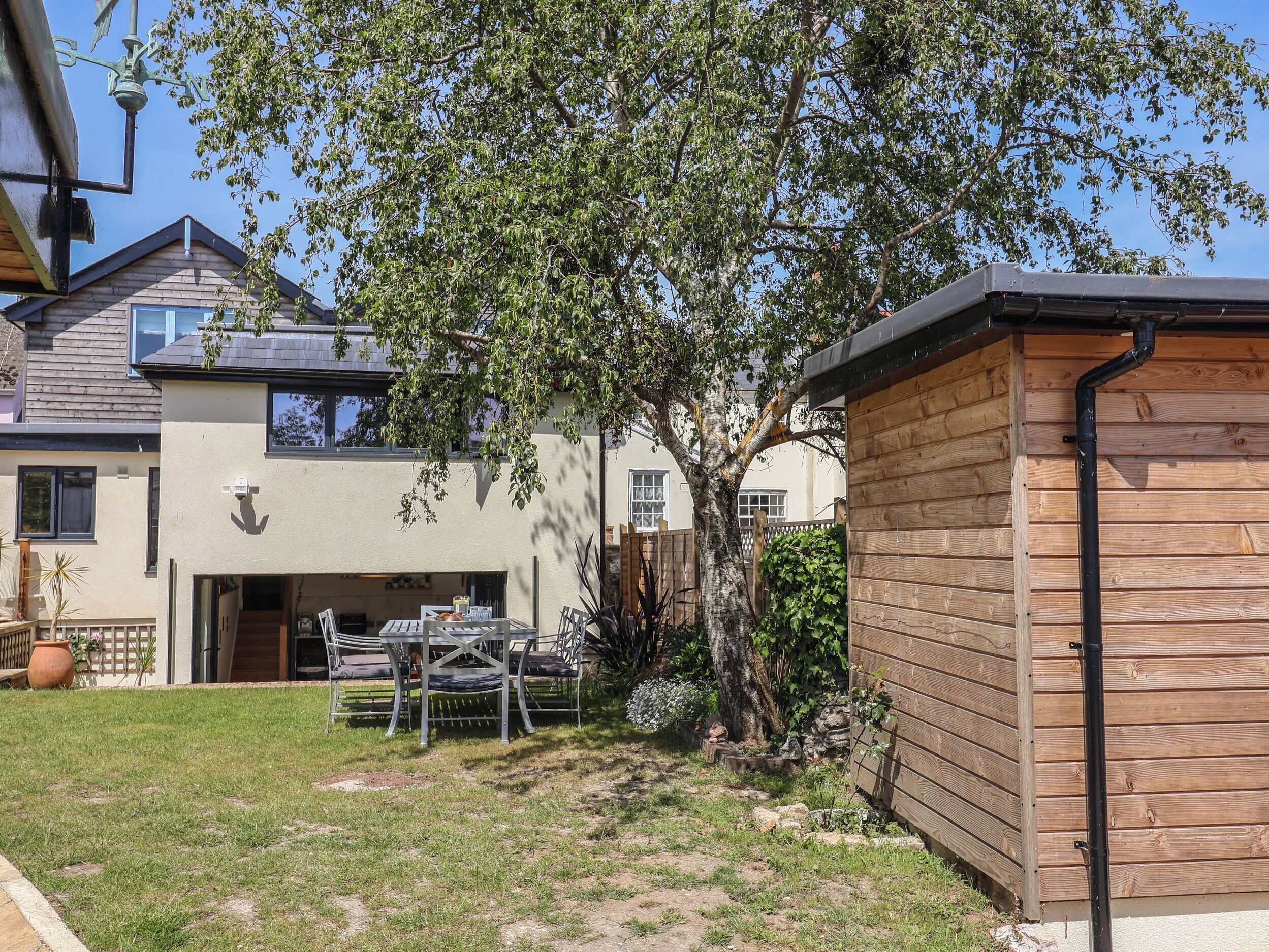 A modern house with a wooden deck, a tree, and a small shed.