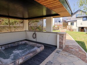 Ein Whirlpool unter einer überdachten Terrasse mit Holzboden, einem Schlauch und Blick auf eine Wohngegend.