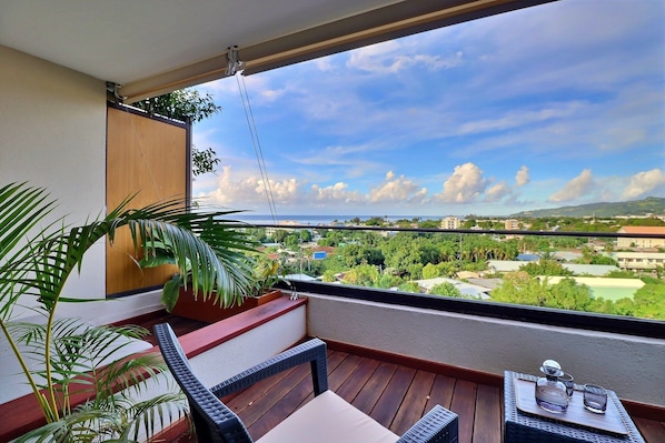 Ein Balkon mit Holzboden, einer hängenden Pflanze, einem Tisch mit einem Glas und einem Stuhl.