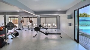 A modern gym with cardio equipment, weightlifting stations, and a view of the ocean through large windows. - Mahana Suite (Papeete)
