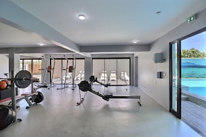 Une salle de sport moderne équipée de machines de cardio, de postes d’entraînement en musculation et offrant une vue sur l’océan grâce à de grandes fenêtres.