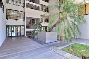 A multi-story building with balconies, large windows, and a central courtyard with plants and a wooden deck. - Mahana Suite (Papeete)