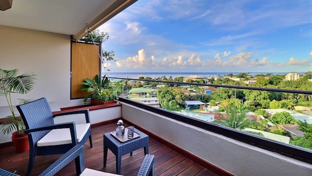 A balcony with a wicker chair, a small table, and potted plants. - Mahana Suite (Papeete)