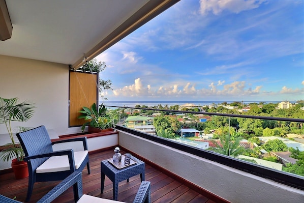 A balcony with a wicker chair, a small table, and potted plants. - Mahana Suite (Papeete)