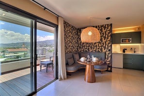 A modern living room with a balcony, a dining table, and a kitchen area. - Mahana Suite (Papeete)