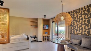 A hotel room with a bed, a sofa, a dining table, a TV, and a large window. - Mahana Suite (Papeete)