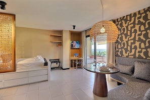 Une chambre d’hôtel avec un lit, un canapé, une table à manger, une télévision et une grande fenêtre.