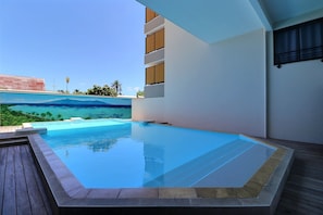 Une piscine avec vue sur un paysage tropical, une terrasse en bois et un bâtiment moderne doté de balcons.