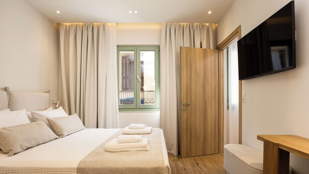 A bedroom with a bed, a wooden bench, a TV, and a door leading to a balcony. - CF Elegant Old Town Suite Fortezza View (Rethymno)