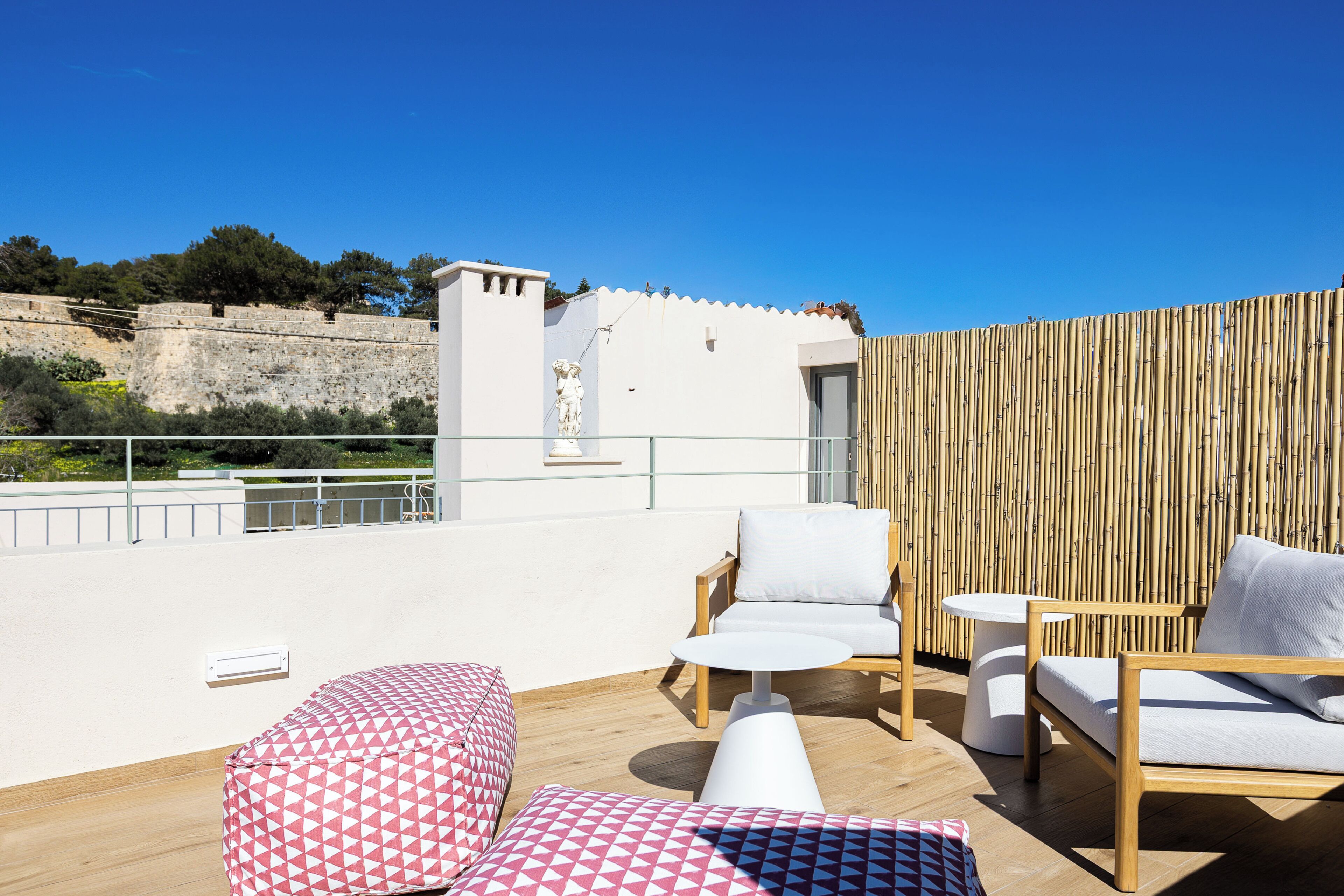 Una terraza en la azotea con muro de piedra, mobiliario de madera y vista a una fortaleza.