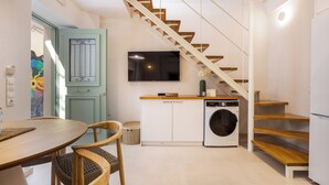 A compact kitchen with a washing machine, wooden staircase, and a dining area with chairs. - CF Elegant Old Town Suite Fortezza View (Rethymno)