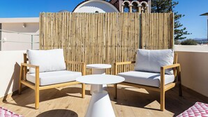 A rooftop terrace with two wooden chairs and a small white table, a bamboo fence, and a building with a dome in the background. - CF Elegant Old Town Suite Fortezza View (Rethymno)