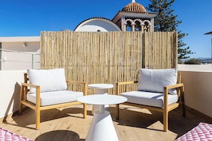A rooftop terrace with two wooden chairs and a small white table, a bamboo fence, and a building with a dome in the background. - CF Elegant Old Town Suite Fortezza View (Rethymno)