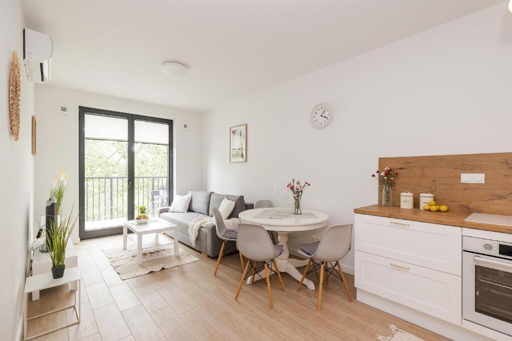 A modern living room with a sofa, dining table, chairs, and a kitchen area with a wooden countertop and cabinets.