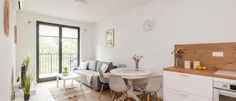 A modern living room with a sofa, dining table, chairs, and a kitchen area with a wooden countertop and cabinets.