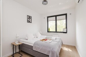 A bedroom with a bed, bedside table, window, and artwork on the wall. - ShortStayPoland Sokratesa (Warszawa)