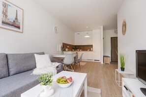 A modern apartment with a grey sofa, a dining area, a kitchen, and a TV. - ShortStayPoland Sokratesa (Warszawa)