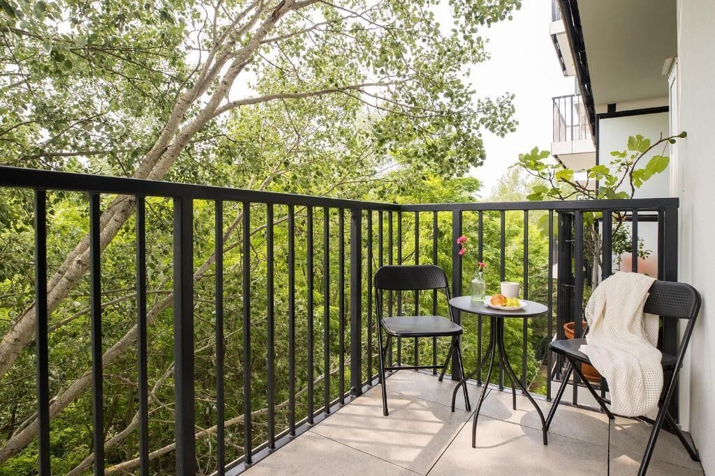 A balcony with a black railing, two chairs, a small round table with a cup and saucer, and a potted plant.