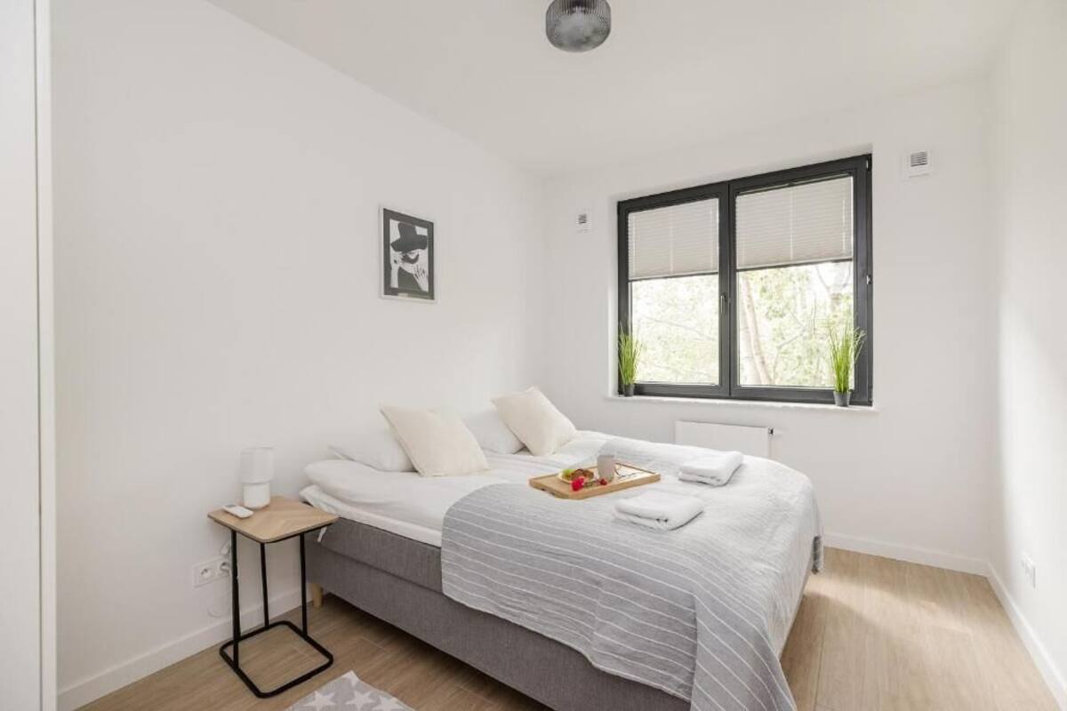 A minimalist bedroom with a bed, bedside table, and a window with blinds.