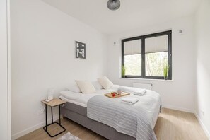 A minimalist bedroom with a bed, bedside table, and a window with blinds. - ShortStayPoland Sokratesa (Warszawa)