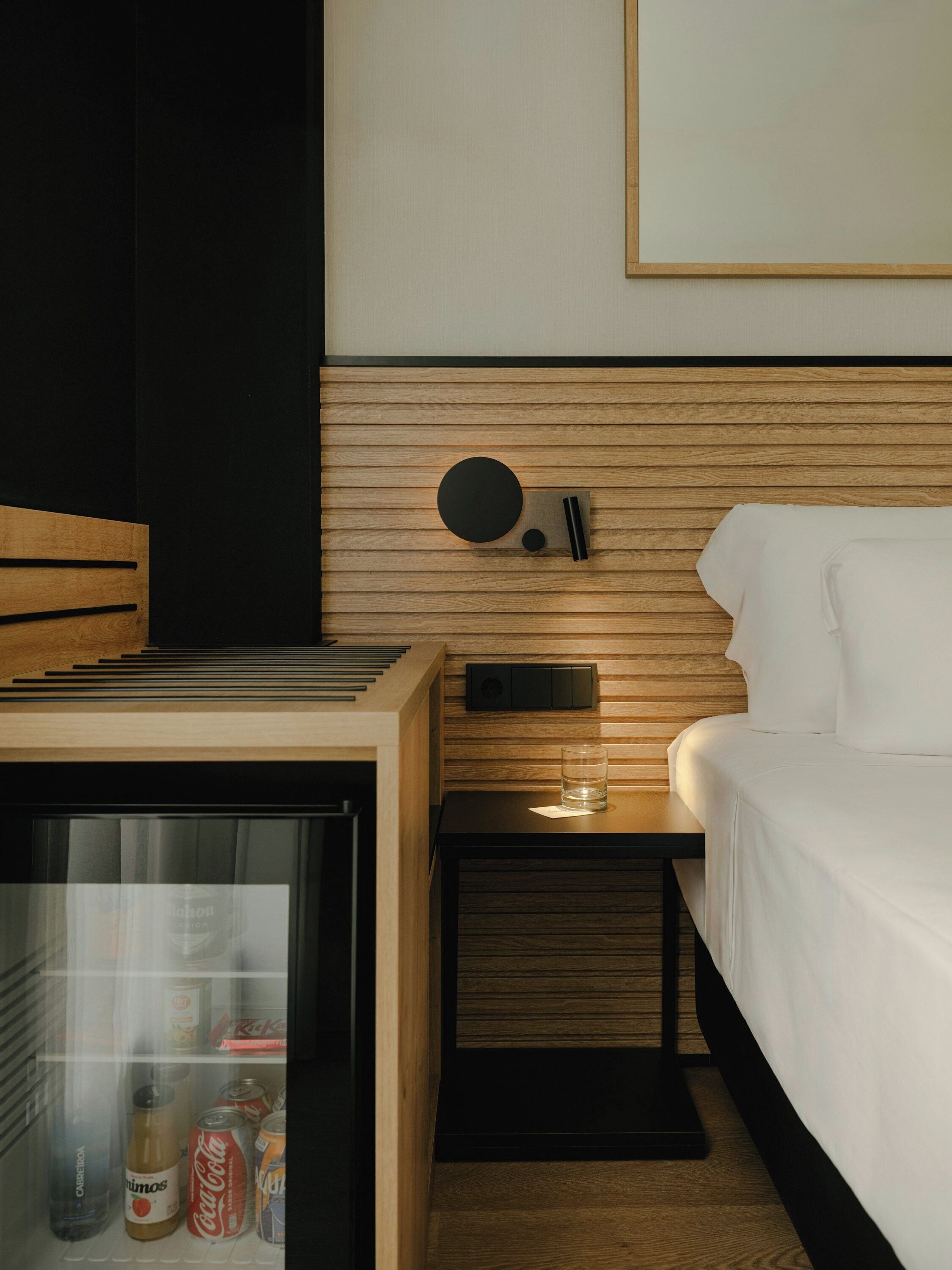 Habitación de hotel con cama, una mesita con un vaso y un minibar.