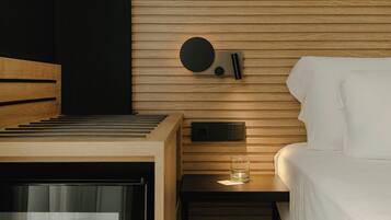 Habitación de hotel con cama, una mesita con un vaso y un minibar.
