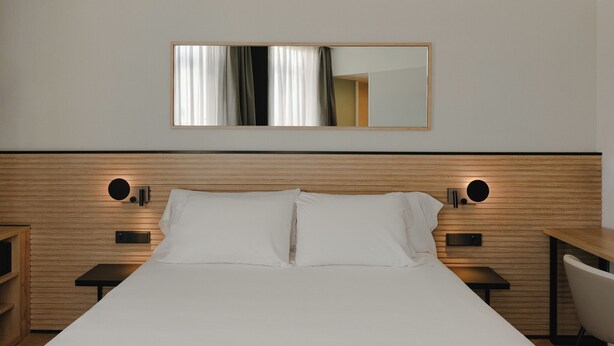 A hotel room with a large bed, bedside tables, a chair, a mirror, and a wooden headboard. - Sercotel Valencia Ruzafa (Valencia)