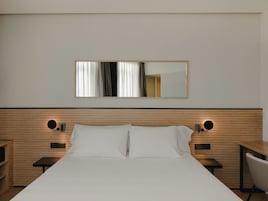 Habitación de hotel con una cama grande, mesitas de noche, una silla, un espejo y un cabecero de madera.