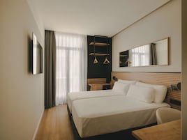 Una habitación de hotel con una cama grande, un escritorio, una silla, un espejo y un armario.