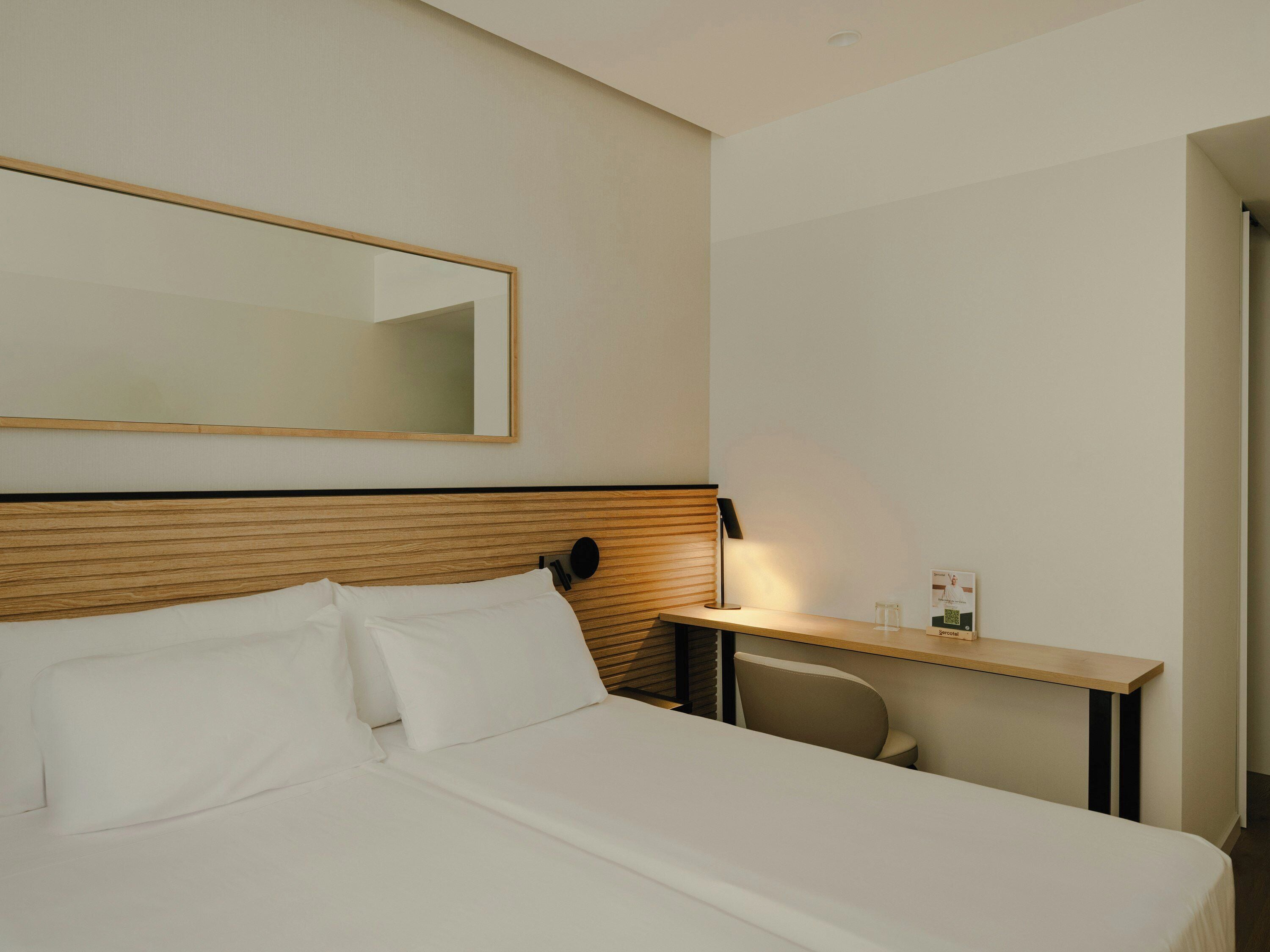 Une chambre d’hôtel comprenant un lit, un bureau, une chaise, un miroir et une lampe.