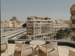 A terrace with a table and chairs, overlooking a cityscape with buildings and a train track.
