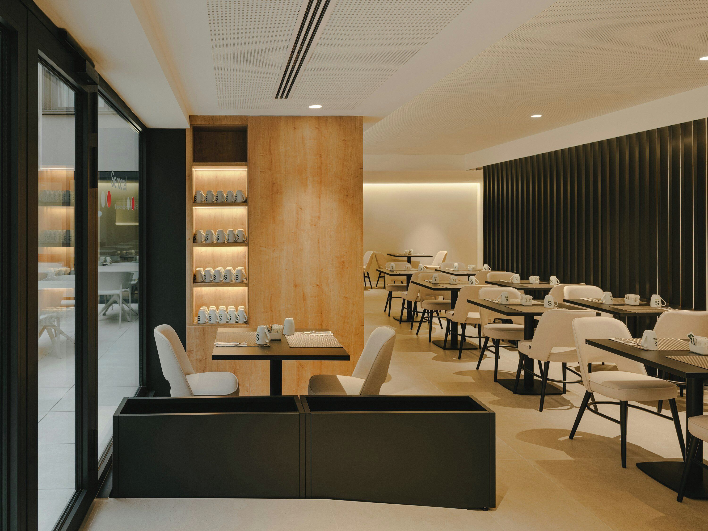 A modern restaurant with a central seating area, a bar, and a view through large windows.
