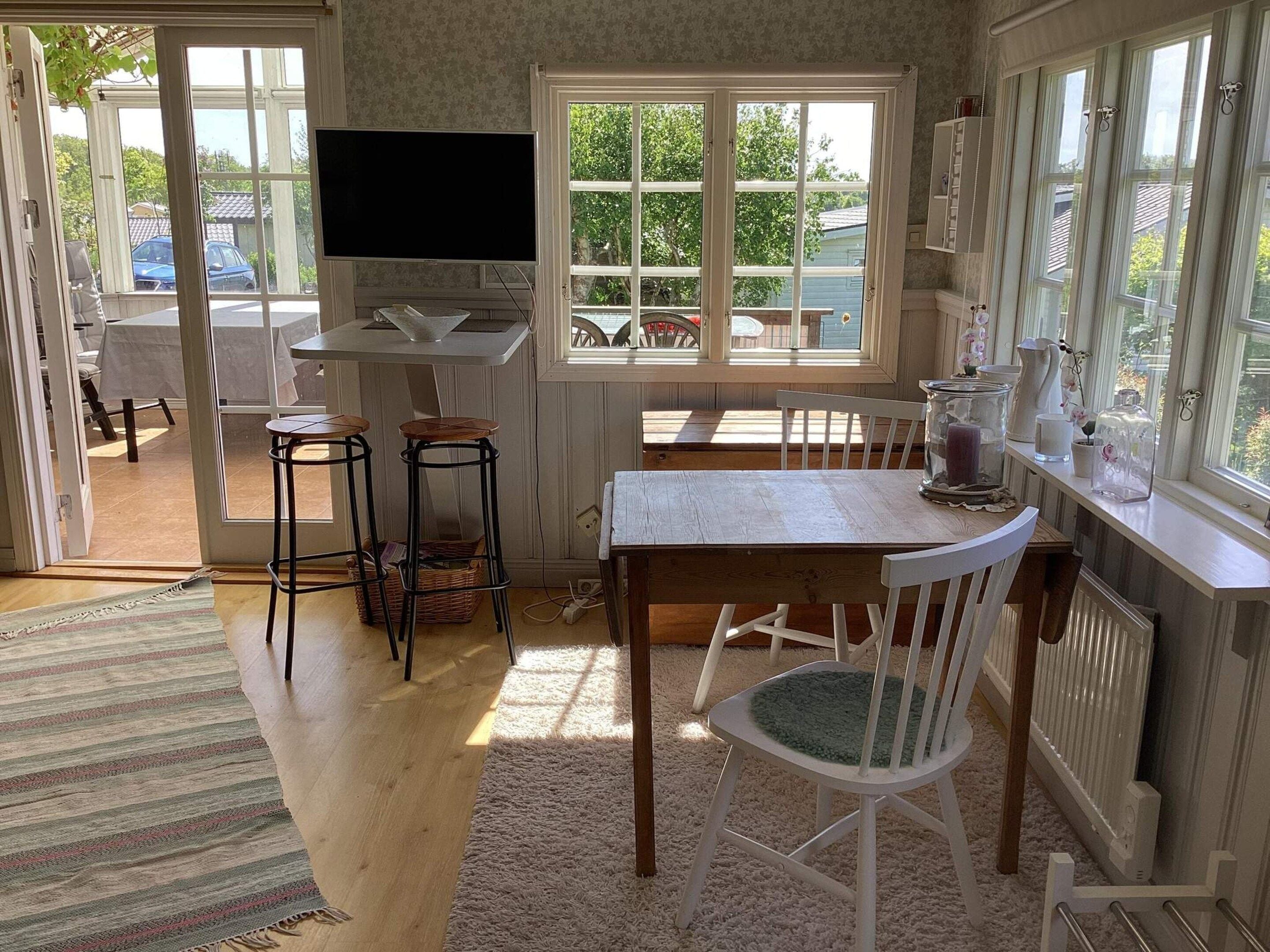 Una cocina con televisor, taburetes de bar, mesa de comedor y ventana con vista al exterior.