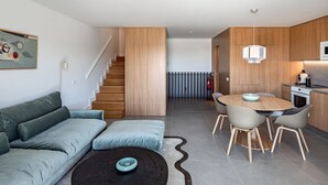 A modern living room with a sofa, a dining table with chairs, a staircase, and a kitchen area. - Ericeira Wave Nest by Lisbeyond (Carvoeira)
